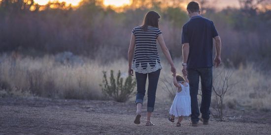 parents holding young daughters hands as she walks
